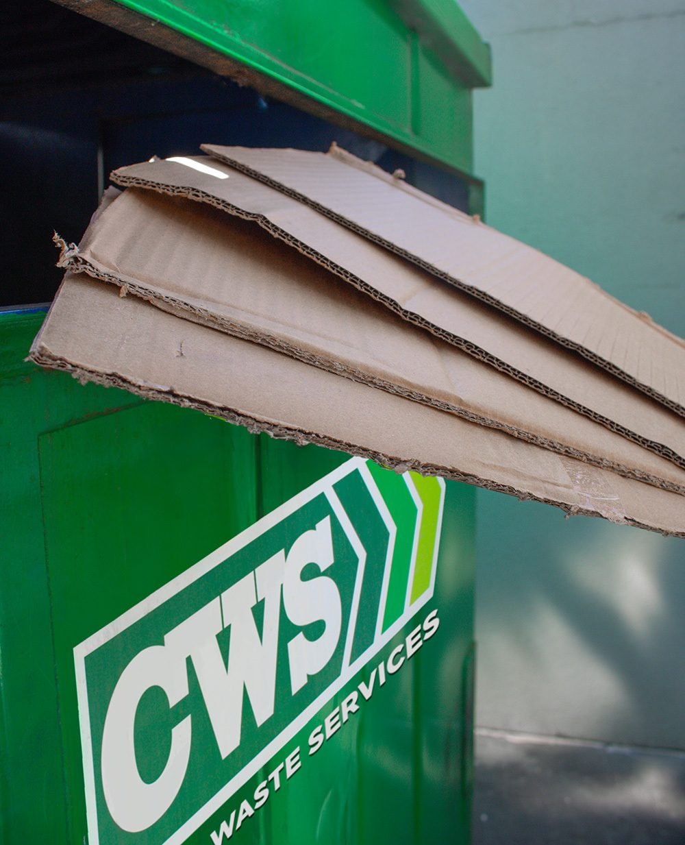 CWS recycling dumpster with a stack of cardboard being put in