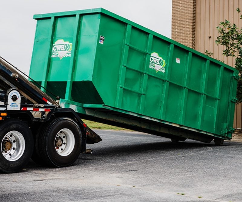 Large dumpster being unloaded from a truck and getting delivered to a business